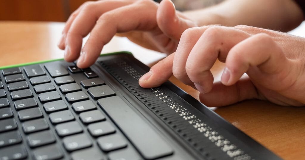 A blind man uses a computer with a Braille display and a computer keyboard.