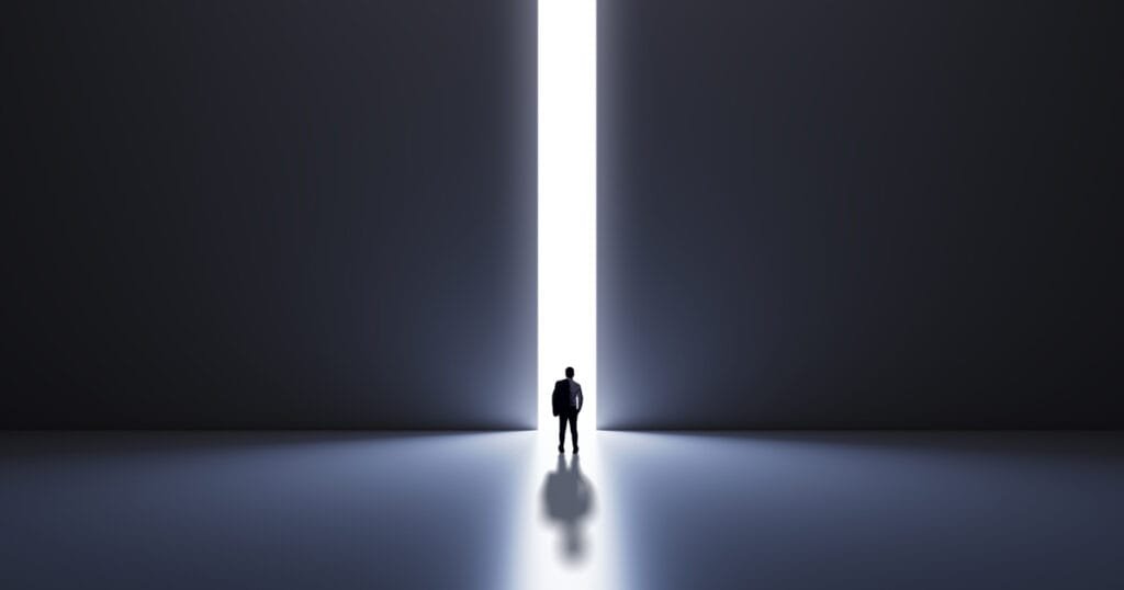 A silhouette of a man stands in a dark room, facing a narrow beam of light that stretches towards the horizon.