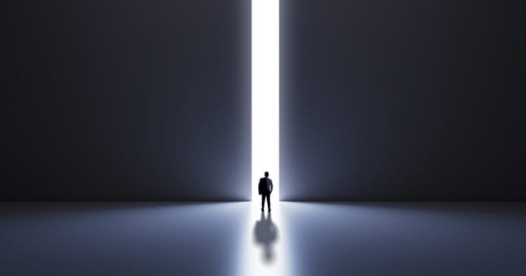 A silhouette of a man stands in a dark room, facing a narrow beam of light that stretches towards the horizon.